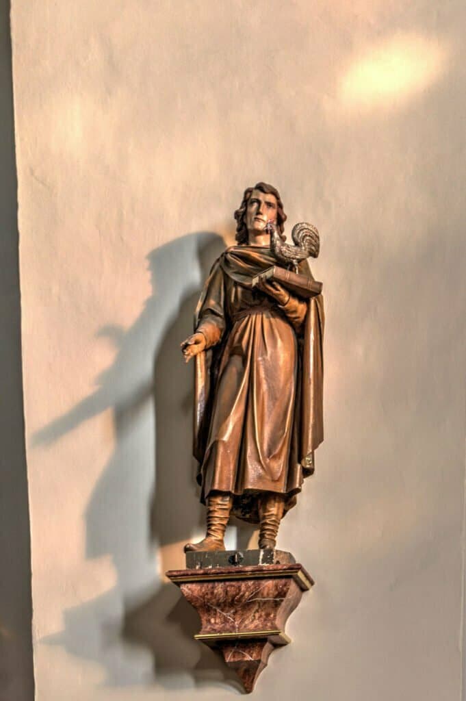 Innenansicht der Kirche in Breitenworbis. Eine männliche Heiligenfigur aus Holz trägt ein Buch mit einem Hahn drauf.