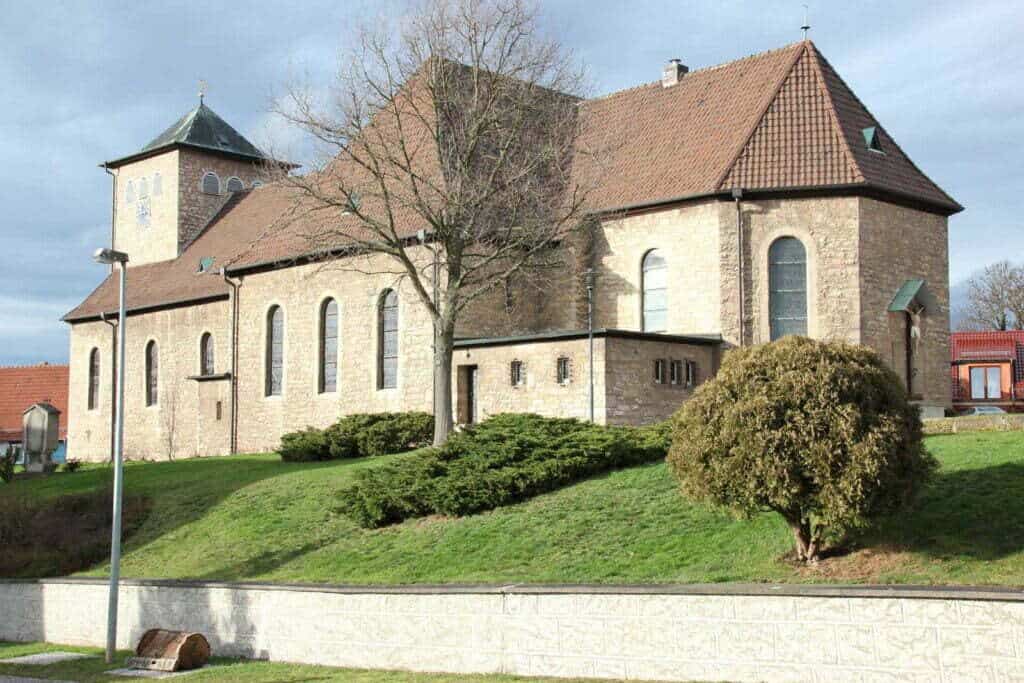 Außenansicht der St. Stephanus Kirche in Gernrode. Zu sehen ein Kirchengebäude, Bäume, Büsche und eine Wiese.